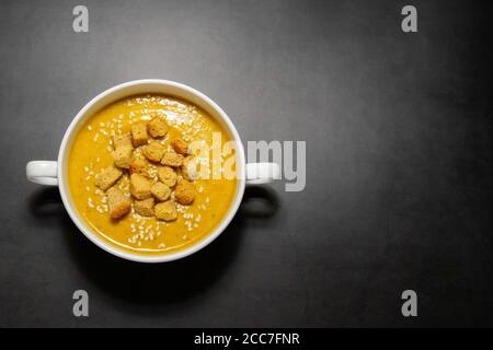 Soupe de crème de citrouille avec craquelins sur fond sombre. Soupe de crème de citrouille avec craquelins dans un bouillon blanc sur fond sombre, assiette pour le texte Banque D'Images