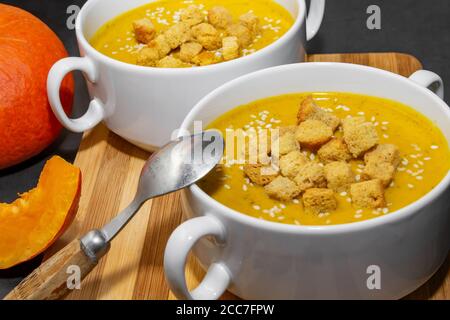 Soupe de potiron d'automne aux graines de sésame sur fond de bois. Deux bols avec soupe d'orange et tranches de citrouille sur le fond Banque D'Images