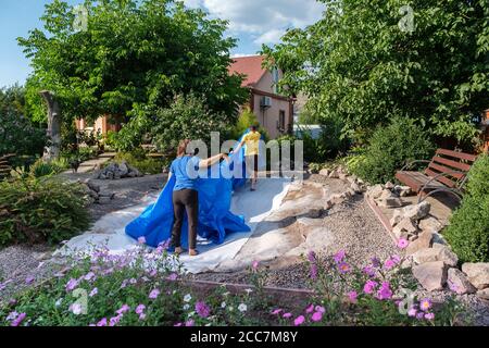 La famille pose une feuille de plastique HDPE bleue sur le sol pour installer un étang à poissons Banque D'Images