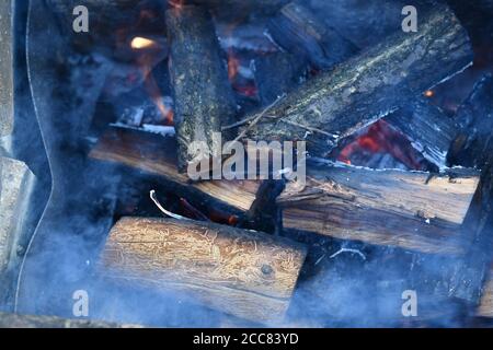 Fumée bleue floue au premier plan de la cheminée provenant du bois de chauffage fumanant et des poutres rouges. Concept traditionnel de chauffage de ferme Banque D'Images