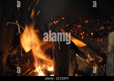 Feu de camp en bois brûlant dans l'obscurité de nuit. Bois de chauffage feu de bois de feu de joie avec des étincelles. Résumé flou de fond de flamme Banque D'Images