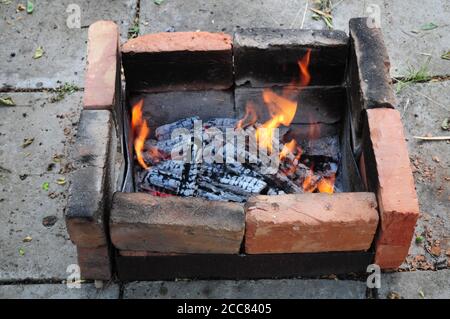 Bois de chauffage brûlé avec une surface noire fissurée recouverte de cendres grises. Briques rouges en terre cuite et fumées charrées dans le vieux charbon de bois mangal parmi l'outdo de ciment Banque D'Images
