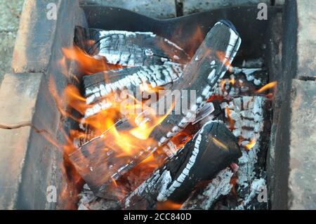 Bois de chauffage avec des flammes sur des bûches fissurées recouvertes de cendres grises. Vieux charbon de bois mangal Banque D'Images