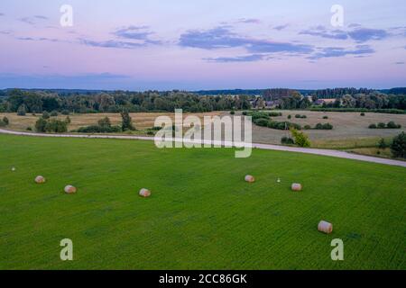 vue aérienne sur les champs avec des rouleaux de blé à l'heure du coucher du soleil, paysage rural avec ciel nuageux fond Banque D'Images