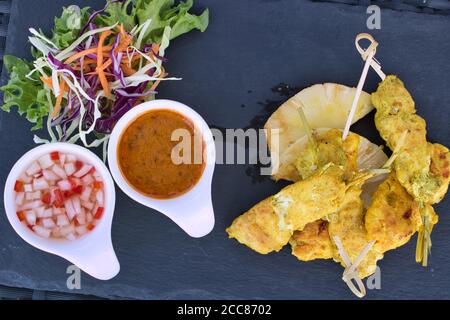 Cette photo unique montre le satay de poulet de départ très élégamment présenté sur une assiette noire avec 2 sauces et une salade. Les brochettes de poulet sont grillées Banque D'Images