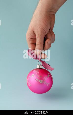 La main mâle tient le ballon de Noël rose. Mâle caucasien adulte avec jouet arbre de Noël en verre. Personne réelle. Concept Noël, nouvel an. Vue latérale. Banque D'Images