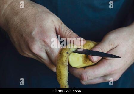 Un homme mûr épluche des pommes de terre crues avec un couteau de cuisine. Gros plan des mains d'un homme du Caucase. Processus de préparation des aliments. 44 ans. Sélectif f Banque D'Images