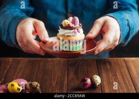 Mains tenant le cupcake de Pâques décoré avec des oeufs de bonbons dans le nid Banque D'Images