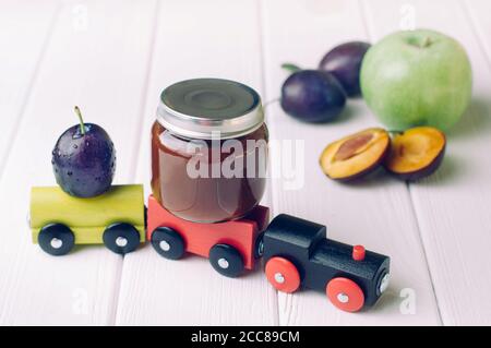 Pot avec purée de prune pour bébé et prune fraîche le train en bois jouet Banque D'Images