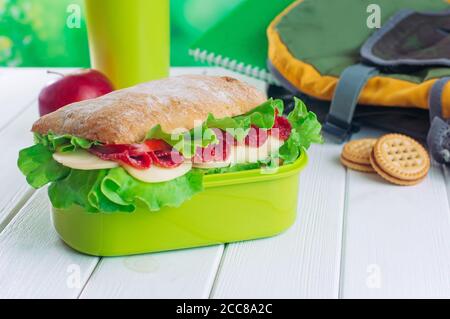 Boîte à lunch avec sandwich près du sac à dos de l'école sur fond blanc Banque D'Images