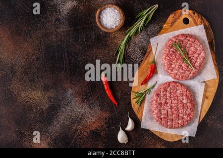 Hamburgers de bœuf frais, hachés et faits maison, sur planche à découper en bois, vue du dessus Banque D'Images