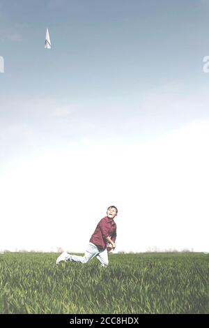 un jeune garçon court dans la prairie en lançant son nouveau papier avion dans les airs Banque D'Images