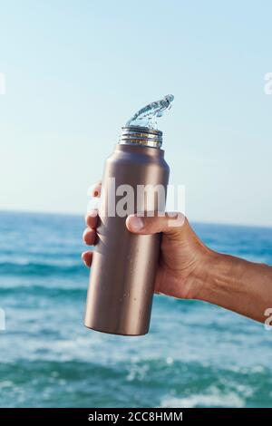 gros plan d'un homme qui verse de l'eau dans une bouteille d'eau réutilisable en aluminium devant l'océan Banque D'Images