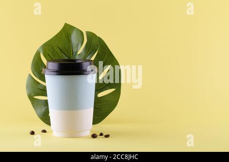 retirez la tasse en papier pour un café avec des grains de café et une feuille de monstère sur fond jaune. espace de copie. concept de café minimal. Banque D'Images