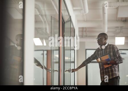 Jeune homme africain en vêtements décontractés ouvrant la porte de la salle du conseil qu'il vient à la réunion Banque D'Images