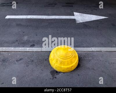 Hémisphère en béton jaune. Limiteur de stationnement et flèche de direction sur l'asphalte. Barrière anti-stationnement sur le trottoir. Photo mobile Banque D'Images