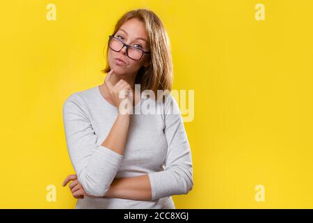 Portrait d'une belle blonde avec des lunettes, qui regarde attentivement. Arrière-plan jaune. Banque D'Images
