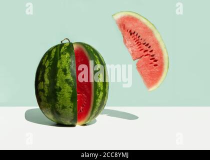 Une grande pastèque fraîche et une tranche de pastèque rouge levitant sur fond de menthe néo. Concept minimaliste créatif de fruits d'été. Banque D'Images