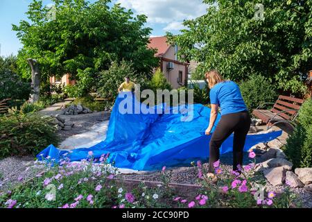 Homme et femme pose une feuille de plastique HDPE bleue le sol pour mettre en place l'étang à poissons Banque D'Images