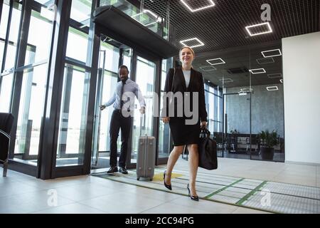 Salutation. Réunion des jeunes partenaires d'affaires après leur arrivée au point de fin de voyage d'affaires. Homme et femme marchant sur un fond de mur de verre d'un bâtiment moderne. Concept d'affaires, finance, publicité. Banque D'Images