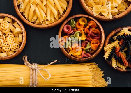 Vue de dessus de l'assortiment de pâtes italiennes colorées dans des bols en bois sur fond noir Banque D'Images