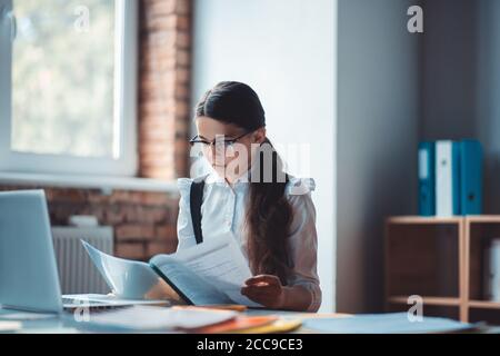 Brunette fille en lunettes de vue lisant un rapport et regardant perturbé Banque D'Images