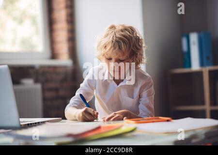 Joli garçon blond assis à la table et écrivant Banque D'Images