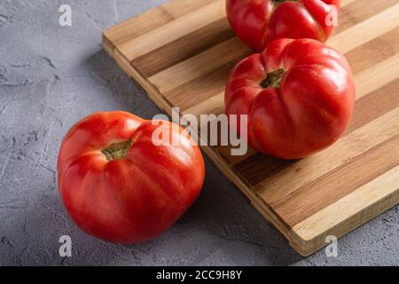 Trois légumes de tomates roses, tomates mûres rouges fraîches sur planche à découper en bois, nourriture végétalienne, fond en béton de pierre, vue d'angle Banque D'Images