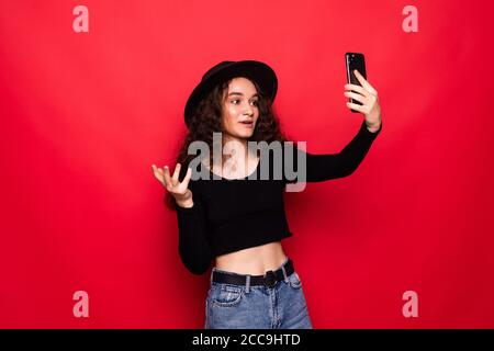Gros plan portrait belle femme prendre selfie sur l'appareil photo avant de smartphone moderne isolé sur fond rouge brillant Banque D'Images
