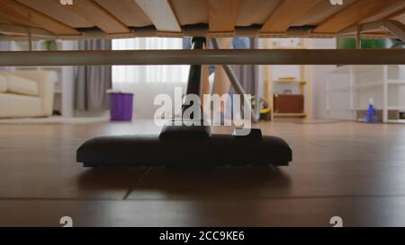 Une femme nettoie la poussière sous un canapé avec un aspirateur. Banque D'Images