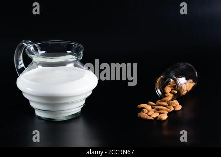 Lait d'amande dans un pot et amandes tombées d'un verre conteneur sur fond noir Banque D'Images