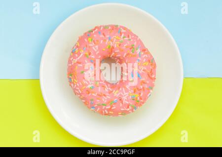 Vue de dessus, donut rose glacé sur plaque blanche sur fond vert pastel turquoise Banque D'Images