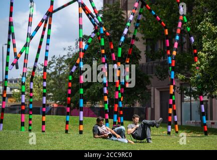 Les gens s'assoient au soleil près de la sculpture « My World and Your World » de l'artiste Eva Rothschild, dans le parc Lewis Cubitt, à Londres, tandis que les gens apprécient le temps chaud après de fortes pluies récentes. Banque D'Images