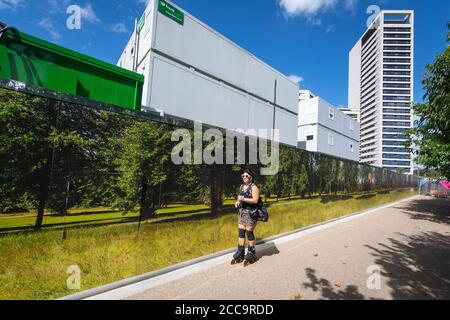 Un rollerblader passe devant une palissade montrant une scène de forêt verte, à l'extérieur d'un chantier dans le nord de Londres, tandis que les gens apprécient le temps chaud après de fortes pluies récentes. Banque D'Images