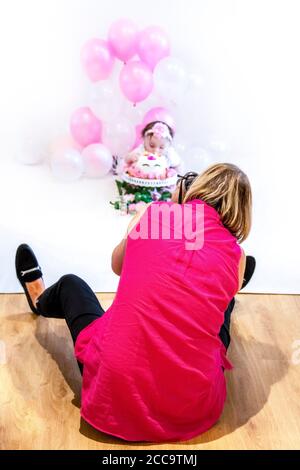 Portrait vertical d'un photographe prenant des photos du gâteau d'une petite fille smash 1ère fête d'anniversaire dans un studio. Banque D'Images