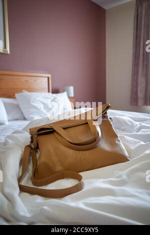 Photographie d'un sac à main sur un lit non fabriqué dans une chambre d'hôtel. Banque D'Images