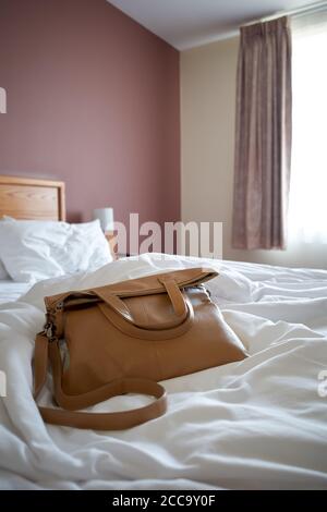 Photographie d'un sac à main sur un lit non fabriqué dans une chambre d'hôtel. Banque D'Images