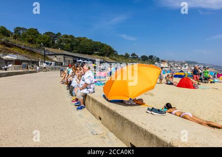 Les touristes obèses assis sur un mur de front de mer manger des icecreams, Lyme Regis, une station balnéaire populaire de vacances sur la côte jurassique, Dorset, SW Angleterre Banque D'Images