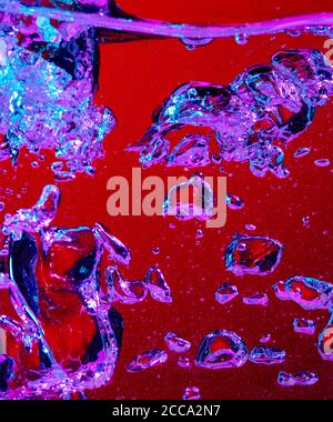 Vue rapprochée du cola froid et frais avec des bulles lumineuses dans la lumière du néon. Texture de la boisson rafraîchissante de l'été avec des bulles macro sur le verre. Se figer ou flotter jusqu'au sommet de la surface, éclaboussures de liquide. Banque D'Images