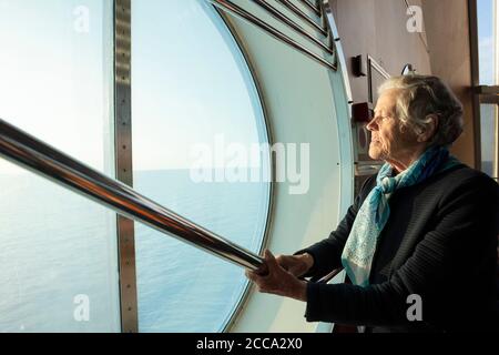 Une femme âgée regarde malheureusement la mer à travers le hublot du ferry. Concept: vie privée, prendre soin des retraités seuls. Photo de haute qualité Banque D'Images