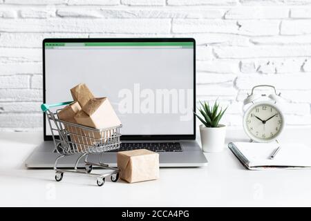 Boîtes dans un chariot sur une table avec ordinateur portable dans un intérieur moderne. Concept d'achat en ligne. Banque D'Images