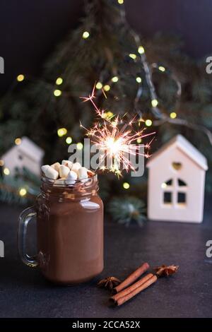 Chocolat chaud dans un pot de maçon en verre avec guimauves, épices et sparkler sur table noire entourée de sapin, de lumières de Noël et de décorations. S Banque D'Images