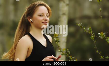 Un mode de vie sain. Jeune femme caucasienne avec casque sans fil en forêt. Prise de vue portrait. Photo de haute qualité Banque D'Images