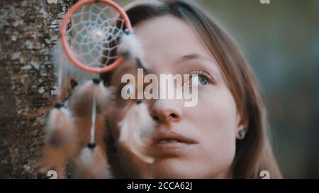 Portrait d'une belle jeune femme caucasienne avec des yeux verts posant dans la forêt près de l'écorce d'arbre avec dreamcatcher devant ses yeux. Photo de haute qualité Banque D'Images
