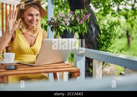 Une femme blonde heureuse salue quelqu'un sur Skype Banque D'Images