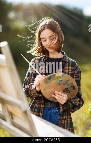 Portrait d'une jeune femme artiste mélangeant de la peinture sur un palette sur une soirée ensoleillée d'été sur un pliner Banque D'Images