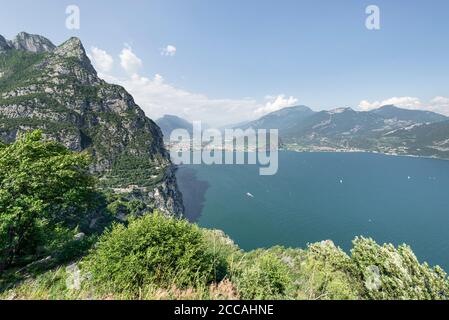 Vue sur les serpentins de l'ancienne route de la Ponale et les falaises rocheuses abruptes du lac de Garde avec le panorama de Riva del Garda et les Alpes, Italie Banque D'Images