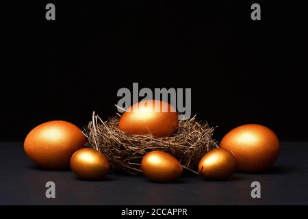 Œufs de Pâques faits main traditionnels peints en couleur dorée à l'intérieur d'un nid d'oiseau isolé sur fond noir. Concept de fête de la famille et du printemps, espace de copie Banque D'Images