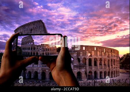 Touriste prenant une photo du Colisée à Rome au coucher du soleil sur un ciel violet nuageux, en Italie. Amphithéâtre ovale romain au crépuscule. Banque D'Images