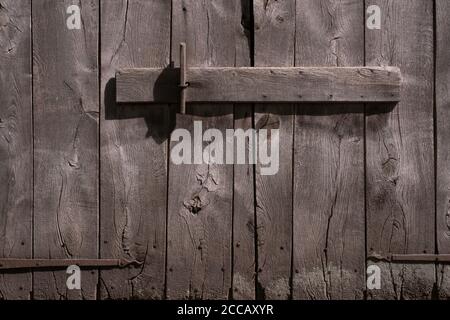 Anciennes portes de grange en bois gris-brun décalées avec charnières en métal rouillé, fermées par une poutre en bois horizontale Banque D'Images